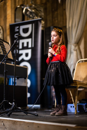 Young girl on stage with a microphone in front of a banner with text