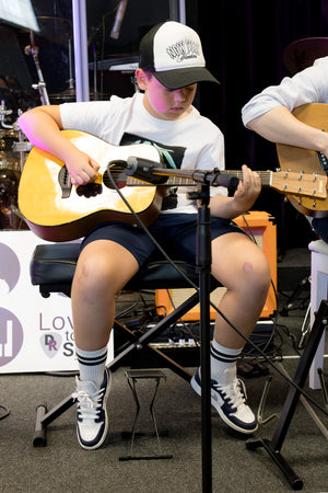 Person playing an acoustic guitar in a casual setting with a microphone stand in front