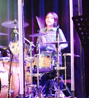 Person playing drums on a stage with musical equipment around